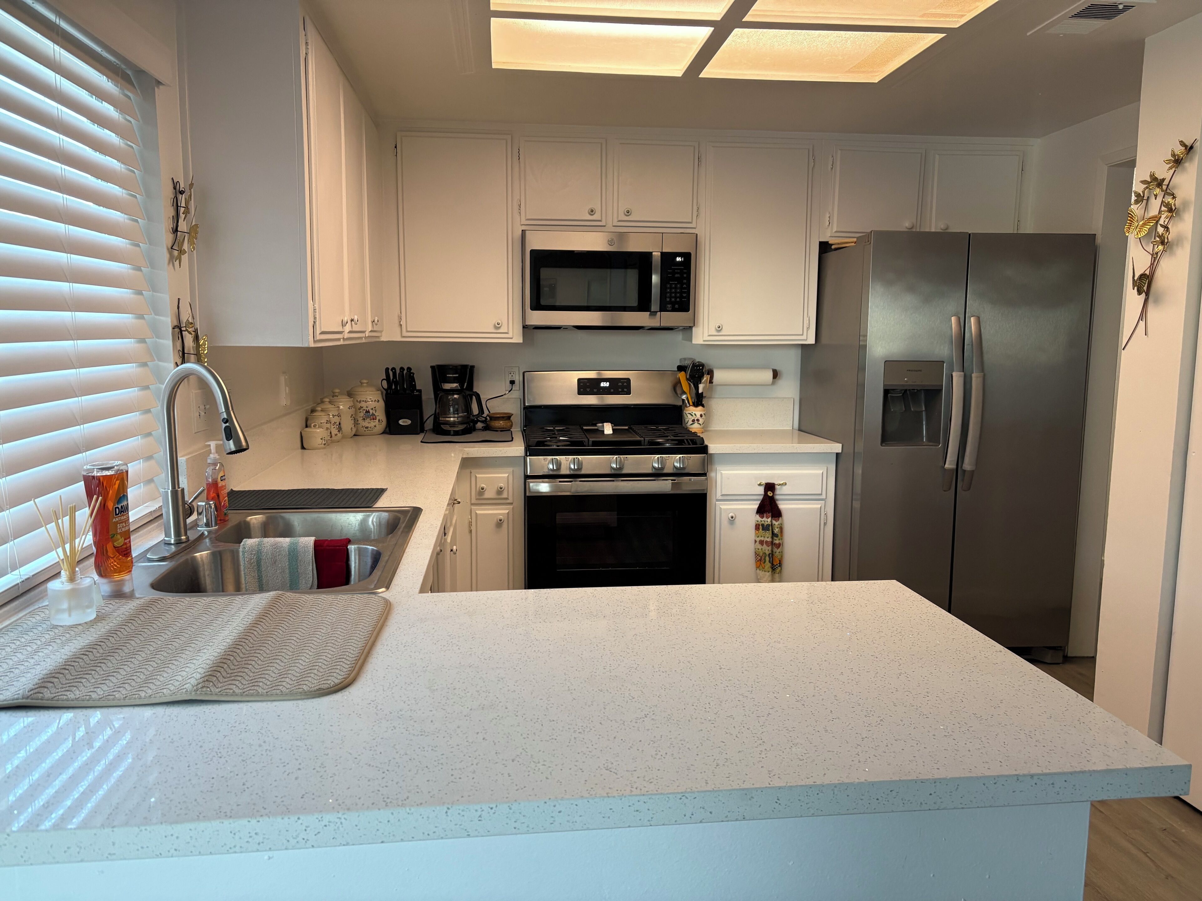 Una cocina moderna con armarios blancos, electrodomésticos de acero inoxidable, microondas integrado, estufa a gas y refrigerador.
