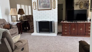 A living room with a fireplace, a ceiling fan, and a television.