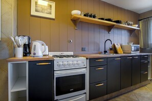 Una cocina con estufa, horno, microondas y estanterías de madera sobre la encimera.
