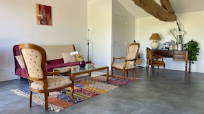 A living room with a sofa, two armchairs, a coffee table, a lamp, a desk, and a guitar.