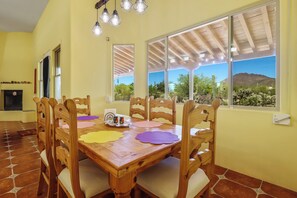 A dining area with a wooden table and chairs, a chandelier, and large windows with a view of cacti and mountains. - Tucson Desert Vacation Home 3BR 2BA Views on 1 Acre Saguaro National Park West (Tucson)
