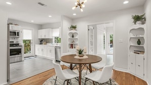 A modern kitchen with white cabinetry, a dining area with a round table and white chairs, and a ceiling light fixture. - Pool Home Oasis - Home for five (Tampa)