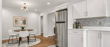 A modern kitchen with white cabinets, a stainless steel refrigerator, and a dining area with a round table and chairs.