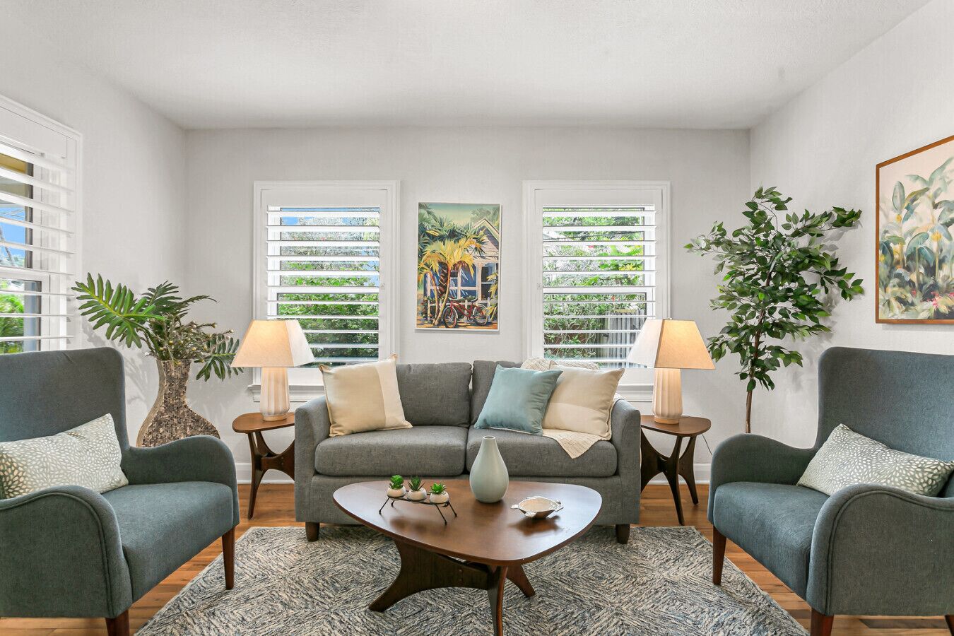 A living room with a grey sofa, two armchairs, a coffee table, and a large window with blinds.
