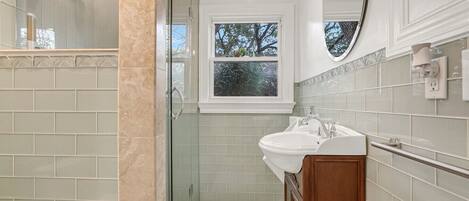A bathroom with a glass shower enclosure, a sink with a vanity, and a window with a view of trees.
