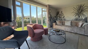 Ein modernes Wohnzimmer mit Sofa, Sessel und Couchtisch, großen Fenstern und Blick auf Grünflächen.
