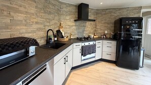 Eine moderne Küche mit einer Rückwand aus Stein, einer schwarzen Dunstabzugshaube, einem eingebauten Backofen und einem schwarzen Kühlschrank.