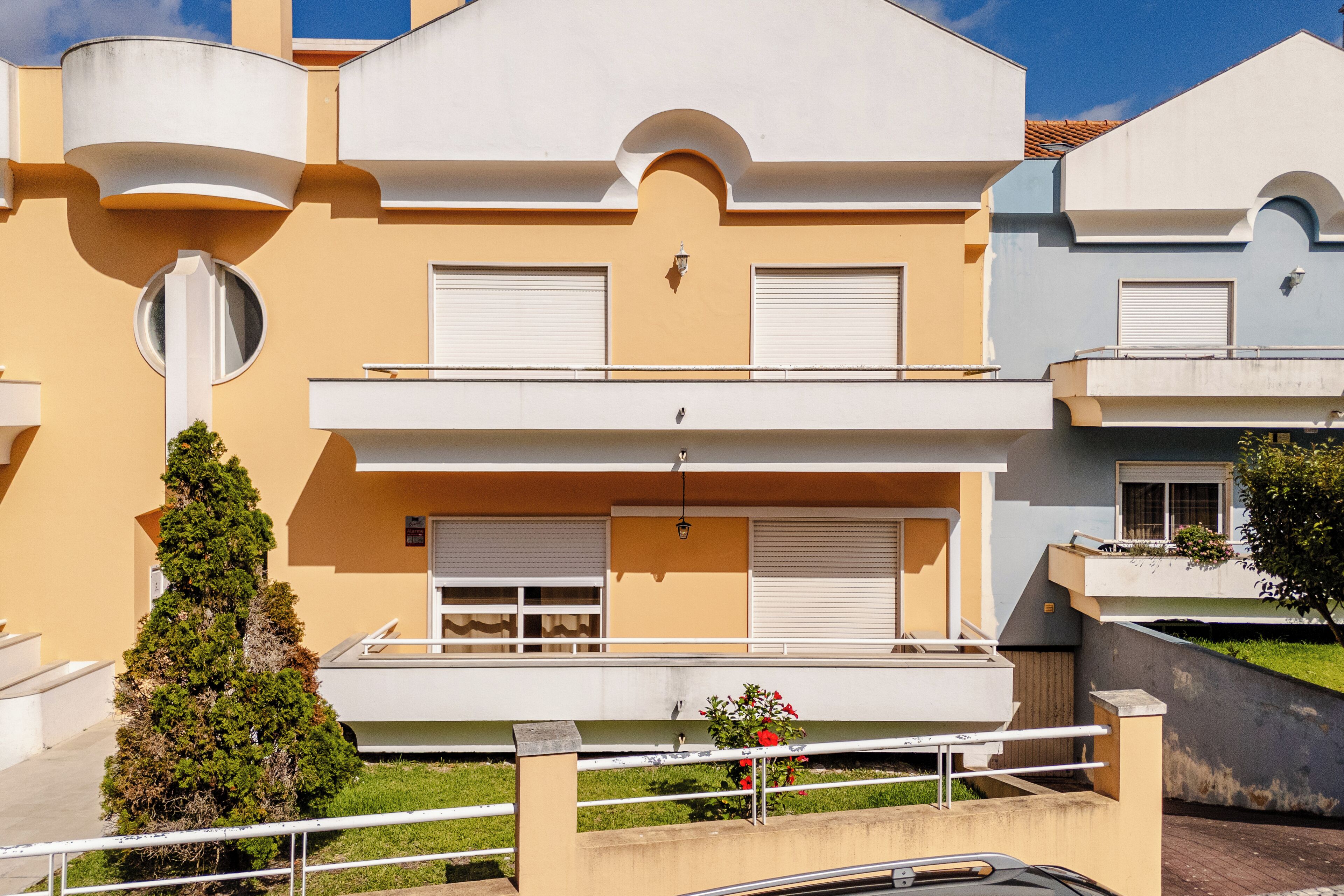 A modern apartment building with balconies, a central courtyard, and a small tree.