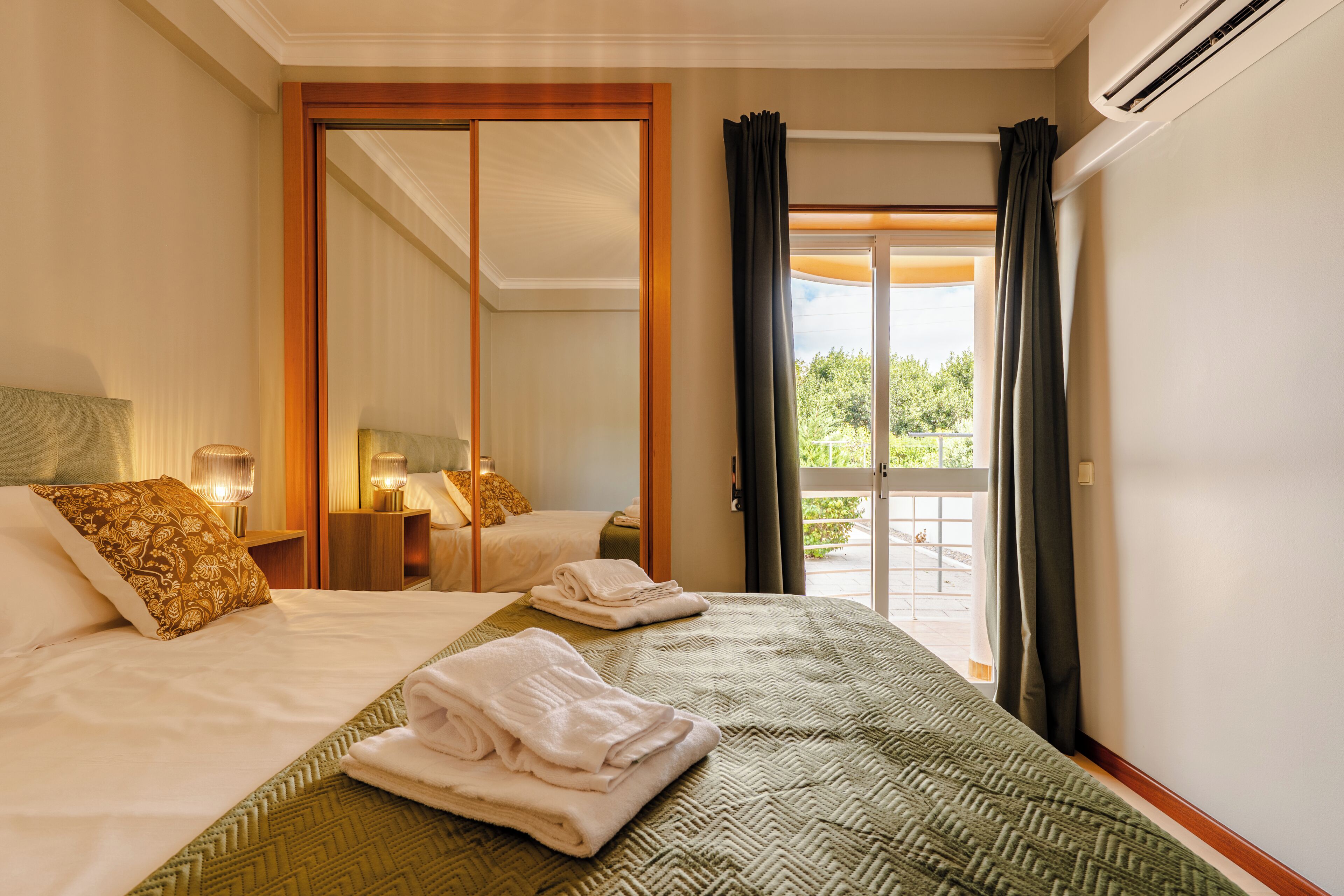 Ein Hotelzimmer mit Bett, Spiegel, Nachttisch und Blick ins Freie.