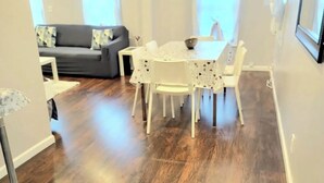 Un comedor con una mesa redonda y sillas, un sofá gris al fondo y suelo de madera.