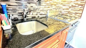 Una cocina con encimera de granito, pileta de acero inoxidable y estufa a gas.