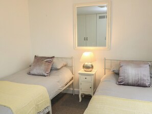 A twin bedroom with two beds, a bedside table with a lamp, a mirror above the beds, and a wardrobe with a small window. - Bosun's Deck (Christchurch)