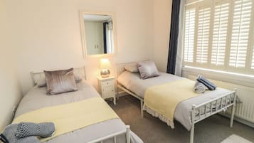Quarto com duas camas de solteiro, mesa de cabeceira com luminária, espelho e janela com persianas.