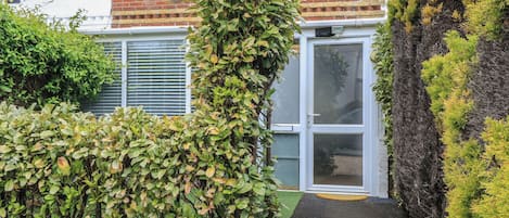 Una propiedad residencial con fachada de ladrillo, una puerta blanca y un pequeño jardín con un sendero de grava que conduce a la puerta.