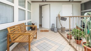 Un balcon avec un banc en bois, des plantes en pot et une vue sur l’intérieur.