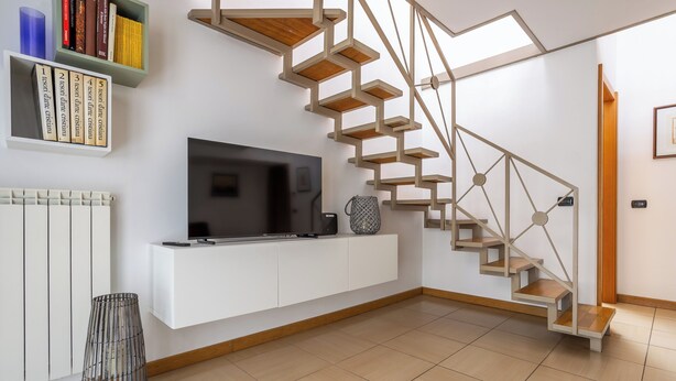 Un salon moderne doté d’un téléviseur encastré, d’une console blanche, d’un escalier aux lignes géométriques et d’une bibliothèque remplie de livres.