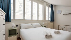 Une chambre d’hôtel comprenant un lit, deux tables de chevet avec des lampes, une fenêtre avec des rideaux et un climatiseur fixé au mur.