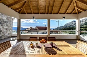 Une pièce spacieuse avec une table en bois dressée pour le repas, de grandes fenêtres offrant une vue sur les montagnes et un mur en pierre.