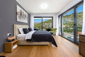 Ein modernes Schlafzimmer mit einem großen Bett, einem Nachttisch, einem Sessel und einem Balkon mit Landschaftsblick.