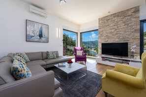 Ein modernes Wohnzimmer mit einer Couch, Sesseln, einem Couchtisch und einem Fernseher.