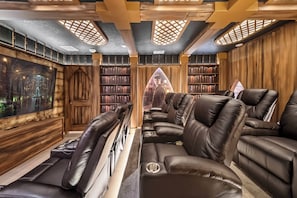 Une salle de cinéma privée avec des fauteuils inclinables en cuir, un grand écran et des étagères à livres.