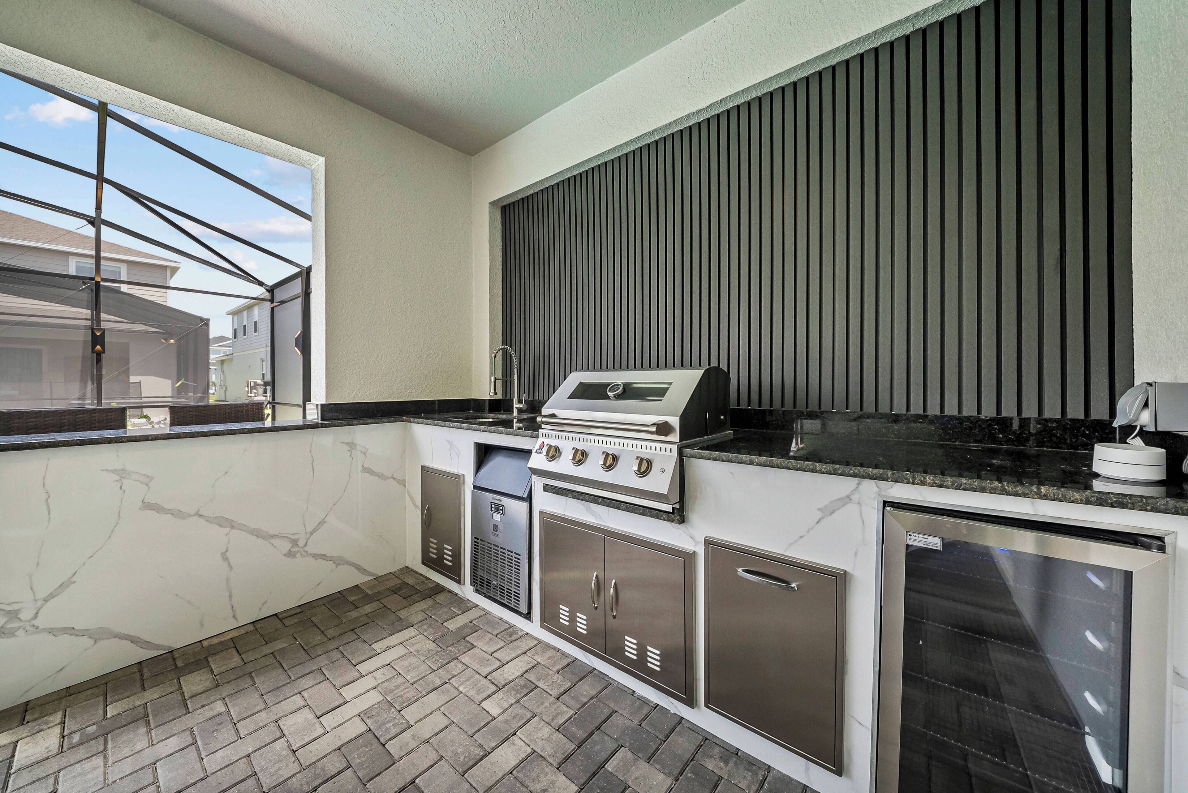 A compact kitchen with a built-in grill, a refrigerator, and a window overlooking a residential area.