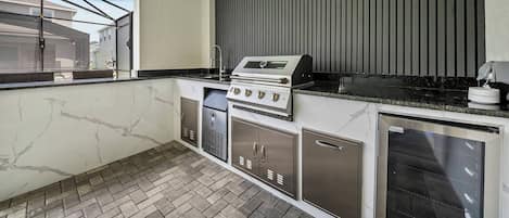 A compact kitchen with a built-in grill, a refrigerator, and a window overlooking a residential area.
