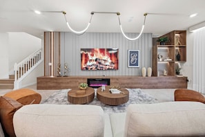 A modern living room with a flat-screen TV, a fireplace, and a staircase. - 10BR house at Windsor Cay Resort (Clermont)