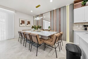 Ein moderner Essbereich mit einem großen rechteckigen Tisch, sechs Stühlen und einer zentral platzierten Vase mit Grünpflanzen.