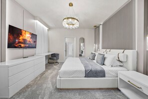 Une chambre moderne avec un grand lit, un téléviseur diffusant une image de cheminée, un lustre et une armoire.