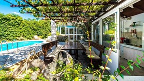 Ein überdachter Außenbereich mit Pool, einem Holztisch und Korbmöbeln.
