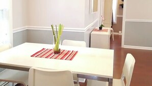 A dining area with a white table, chairs, and a vase of green plants.