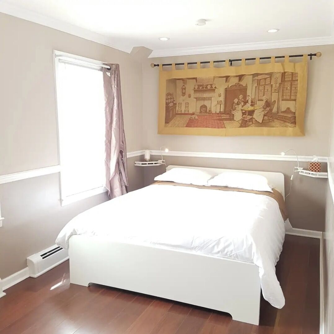 A bedroom with a large bed, a window with curtains, a wall-mounted painting, and a radiator.