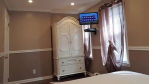 A bedroom with a bed, a dresser, a television mounted on the wall, and a window with curtains.
