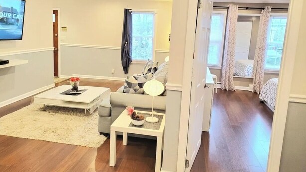 A living room with a sofa, coffee table, and TV. There is a door leading to a bedroom with a bed.