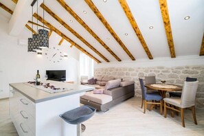 A cozy loft with exposed wooden beams, a stone wall, a sofa, a dining table, and a TV. - Three Bedrom Apartment (Slano)