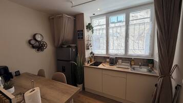 Een kleine keuken met een koelkast, een spoelbak en een raam met gordijnen.