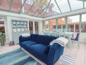 A conservatory with a blue sofa, dining table, and chairs, and a display of plates and cups. - The Beach House (Prestatyn)