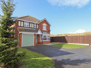 A two-story house with a green garage door, a satellite dish, and a fenced yard. - The Beach House (Prestatyn)