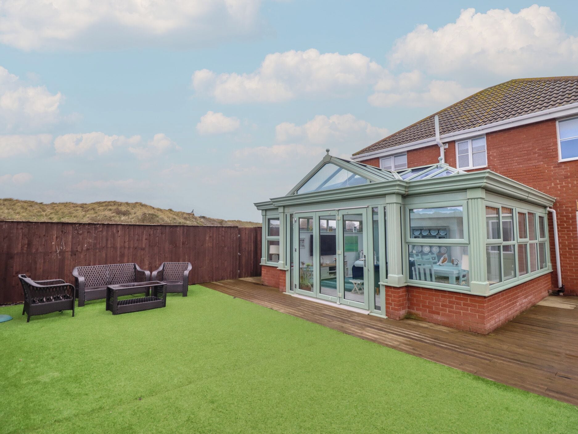 A conservatory with a glass roof, a wooden deck, and a green lawn.