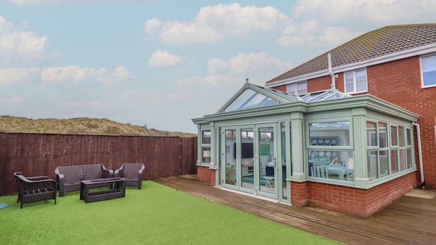 A conservatory with a glass roof, a wooden deck, and a green lawn. - The Beach House (Prestatyn)