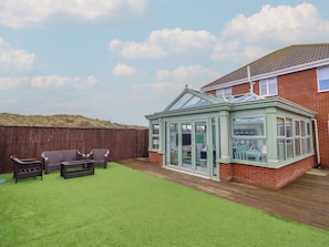 A conservatory with a glass roof, a wooden deck, and a green lawn.