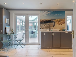 A modern kitchen with a large window, a dining area with chairs, and a view of the beach through the window.
