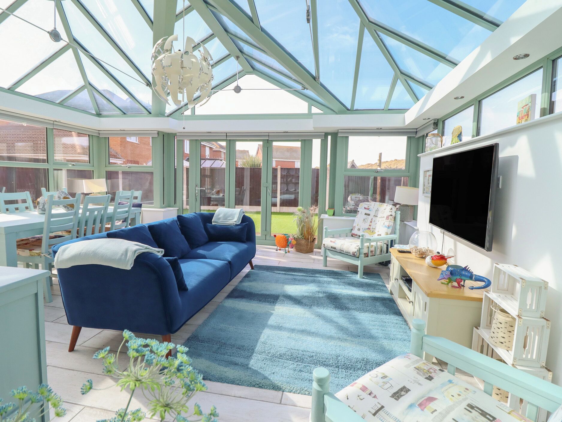 A conservatory with a blue sofa, a dining table, chairs, and a TV.