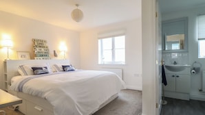 A bedroom with a bed, bedside lamps, a window, and a bathroom visible through an open door. - The Beach House (Prestatyn)