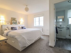 A bedroom with a bed, bedside lamps, a window, and a bathroom visible through an open door. - The Beach House (Prestatyn)