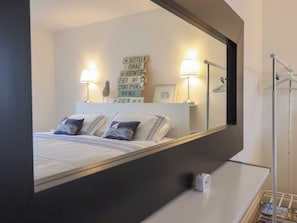 A hotel room with a bed, two bedside lamps, a mirror, a small table, and a wall with decorative signs.