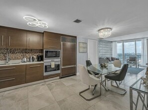A modern kitchen with built-in appliances, a dining area with a glass table, and a city view through large windows. - Icon Brickell - 42nd Fl - Oceanview - Spa Access (Miami)