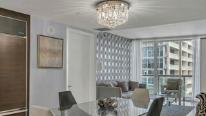 Ein modernes Wohnzimmer mit einem Glastisch, einer Kandelaberleuchte und Blick auf ein Gebäude durch große Fenster.