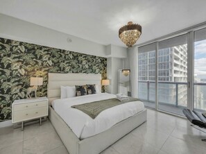 A modern bedroom with a large bed, a nightstand, a mirror, and a view of the city through large windows. - Icon Brickell - 42nd Fl - Oceanview - Spa Access (Miami)